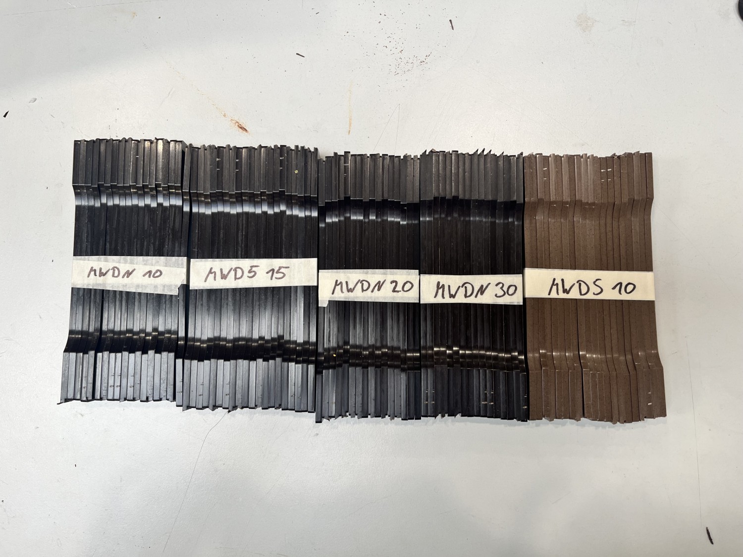 Arrangement von spritzgegossenen GEOBRIS PUPA Schulterstäben für Stresstests, nebeneinander auf einer Fläche ausgelegt und nach Varianten beschriftet.